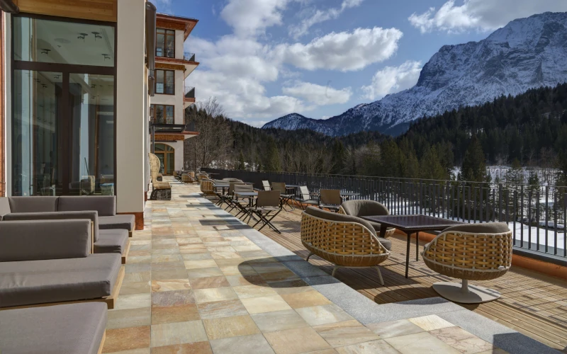 Terrasse mit Sitzmöbeln, Bergblick, sonniges Wetter, entspannte Atmosphäre, ideal für Erholung und Genuss.