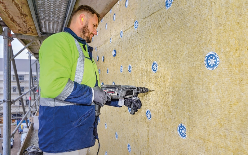 Handwerker bohrt mit einer Bohrmaschine in Dämmung an einer Außenwand