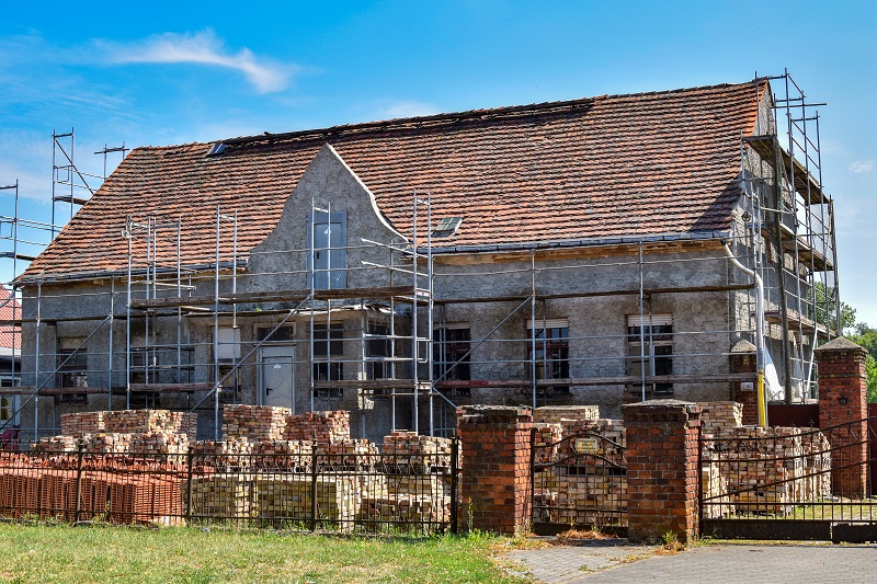 altes Haus in der Fassadensanierung mit großem Gerüst und vielen Steinen davor