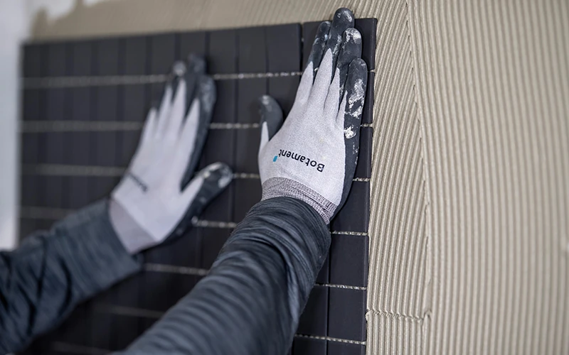 Handwerker bringt Fliesen an einer Wand mit Fliesenkleber an