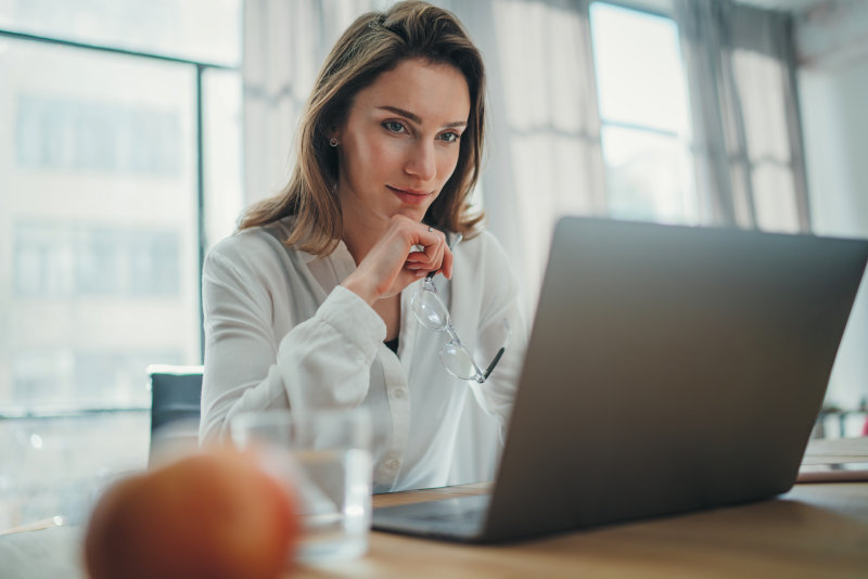 Frau sitzt vor einem Laptop und überlegt etwas