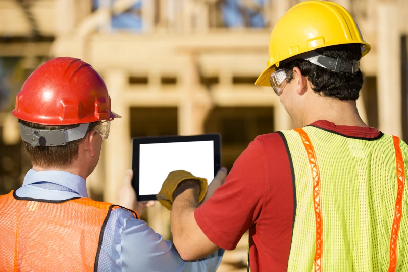 zwei Handwerker in Schutzkleidung auf einer Baustelle schauen auf ein Tablet