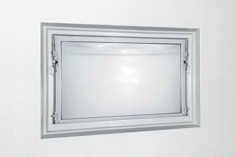Ein weißes, veraltetes Kellerfenster ist zu sehen.