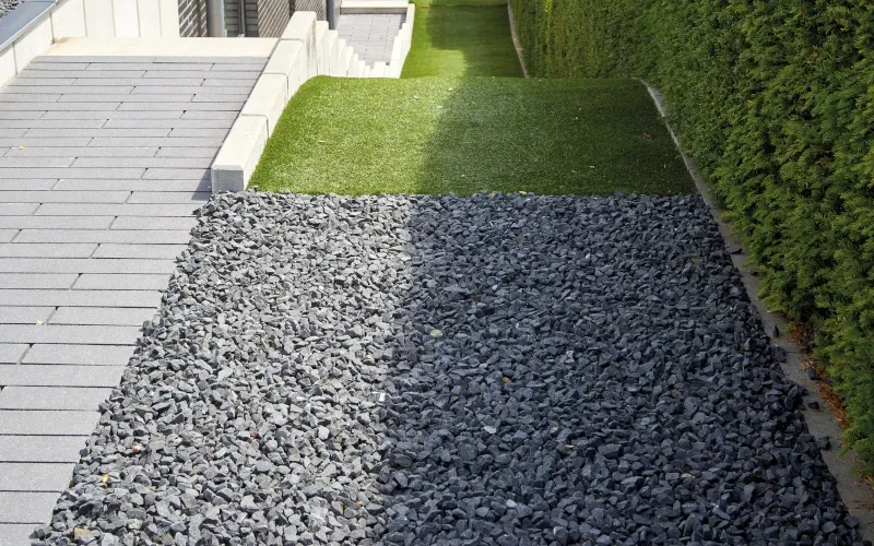 Kiesbeet mit grauem Kies in einem Garten mit grüner Hecke