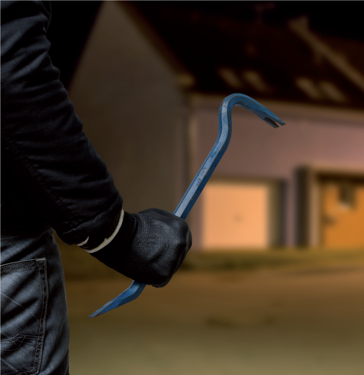 Einbrecher mit Brechstange in der Hand steht nachts vor einem Haus