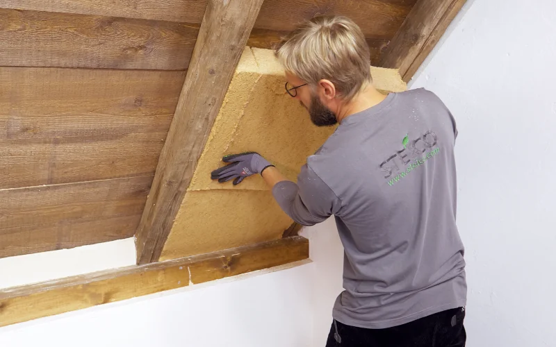 Handwerker drückt Dämmplatten in vorgesehen Konstruktion an Dachschräge