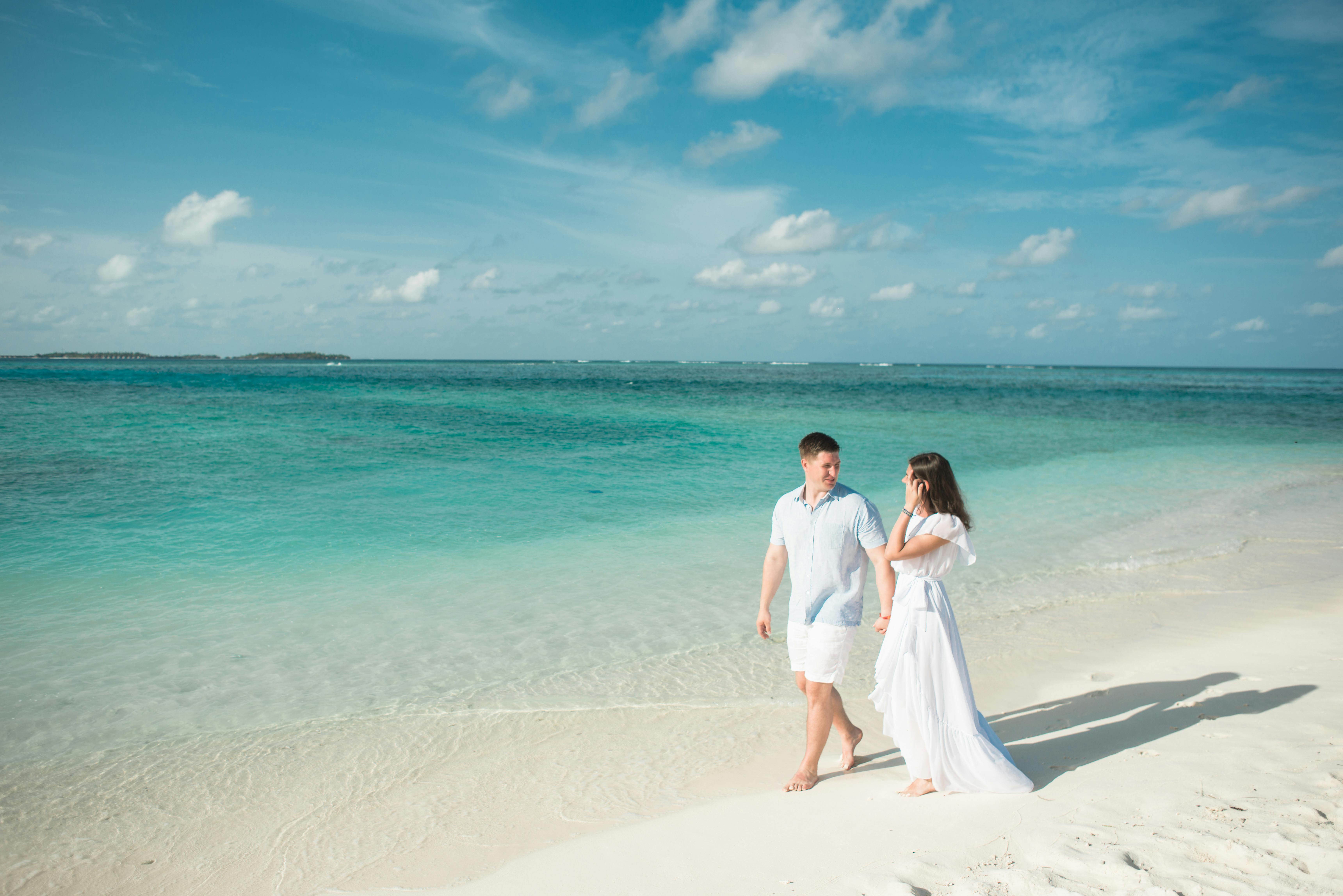 Newlywed couple wearing white on a beautiful white sand beach with blue skies and turquoise waters