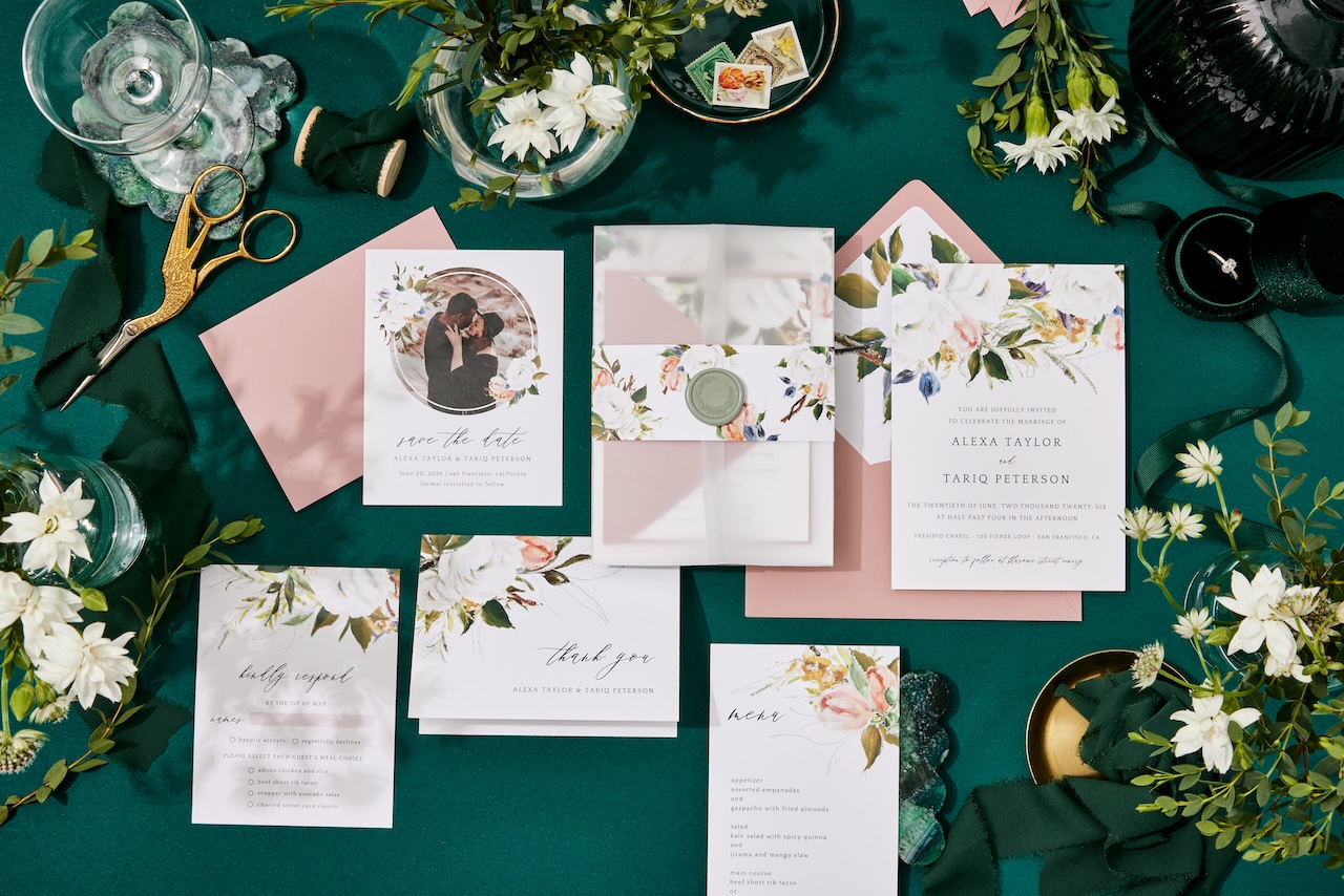 Floral wedding invitation suite laid out on a green table