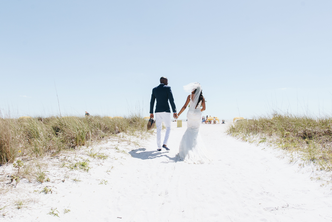 Couple walking hand in hand through a sandy path at a beachside destination wedding