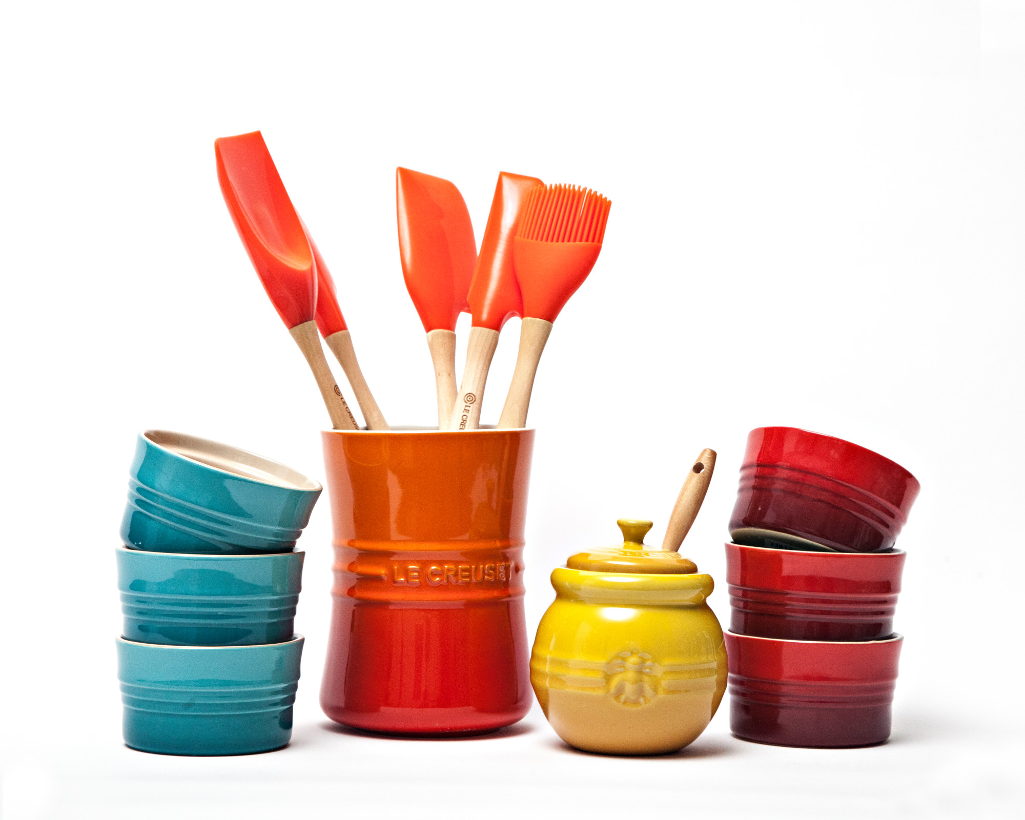 Le Creuset crock with cooking utsensils in flame orange, ramekins in teal blue and red, and honey pot in yellow