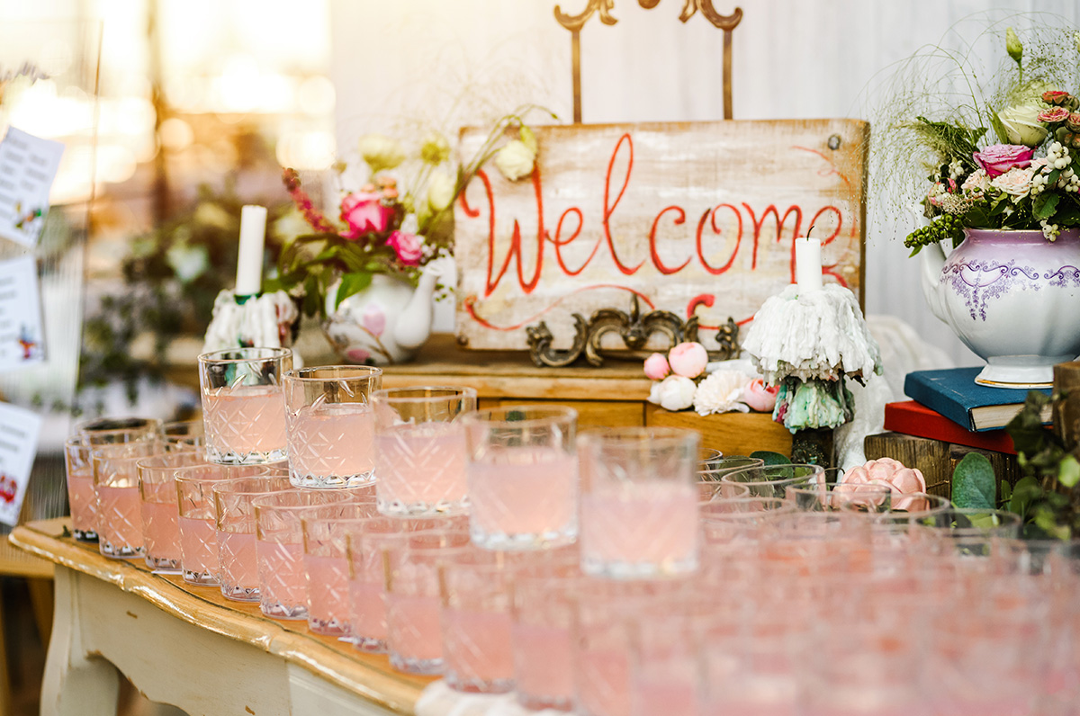 A closeup of a table adorned with flowers and rows of cocktail glasses are shown, alluding to one of the many wedding bar ideas couples can choose from when planning their wedding. 