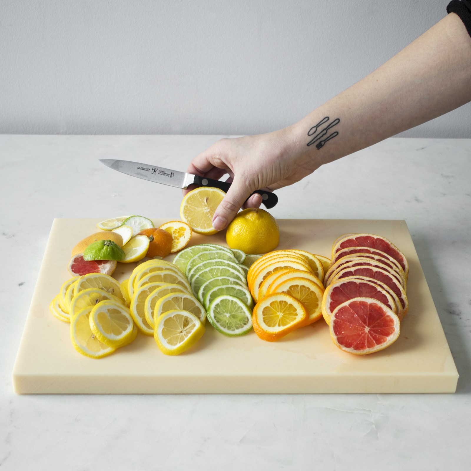 a hand holding a knife and placing lemon on cutting board with yellow, green,orange,red sliced citrus fruits