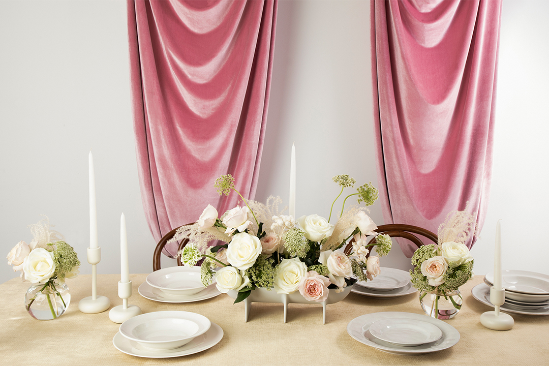 Image of a table with flowers and two place settings with two pink satin curtains hanging behind