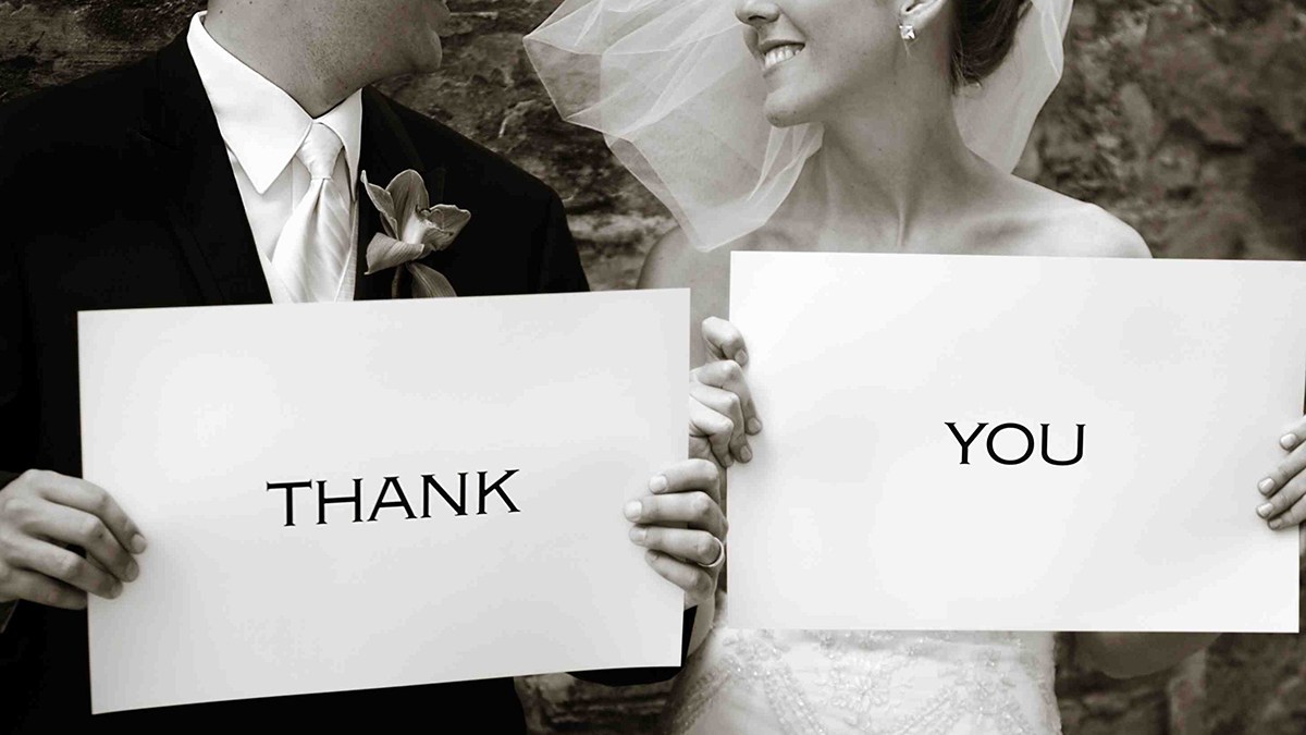 Groom holding white card with Thank  and bride holding card written You