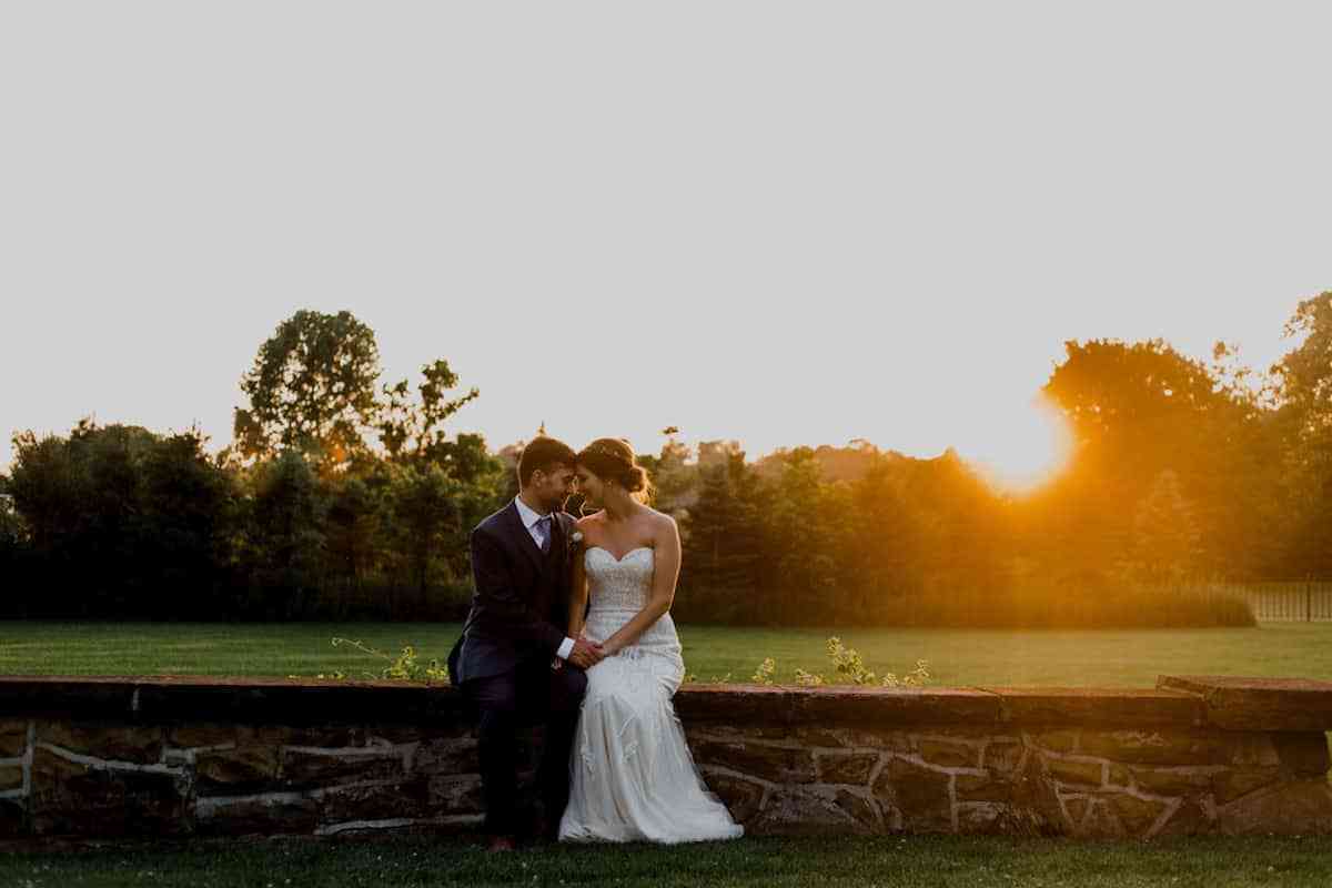 Bride and groom sitting side by side outdoors in wedding attire as the sun sets