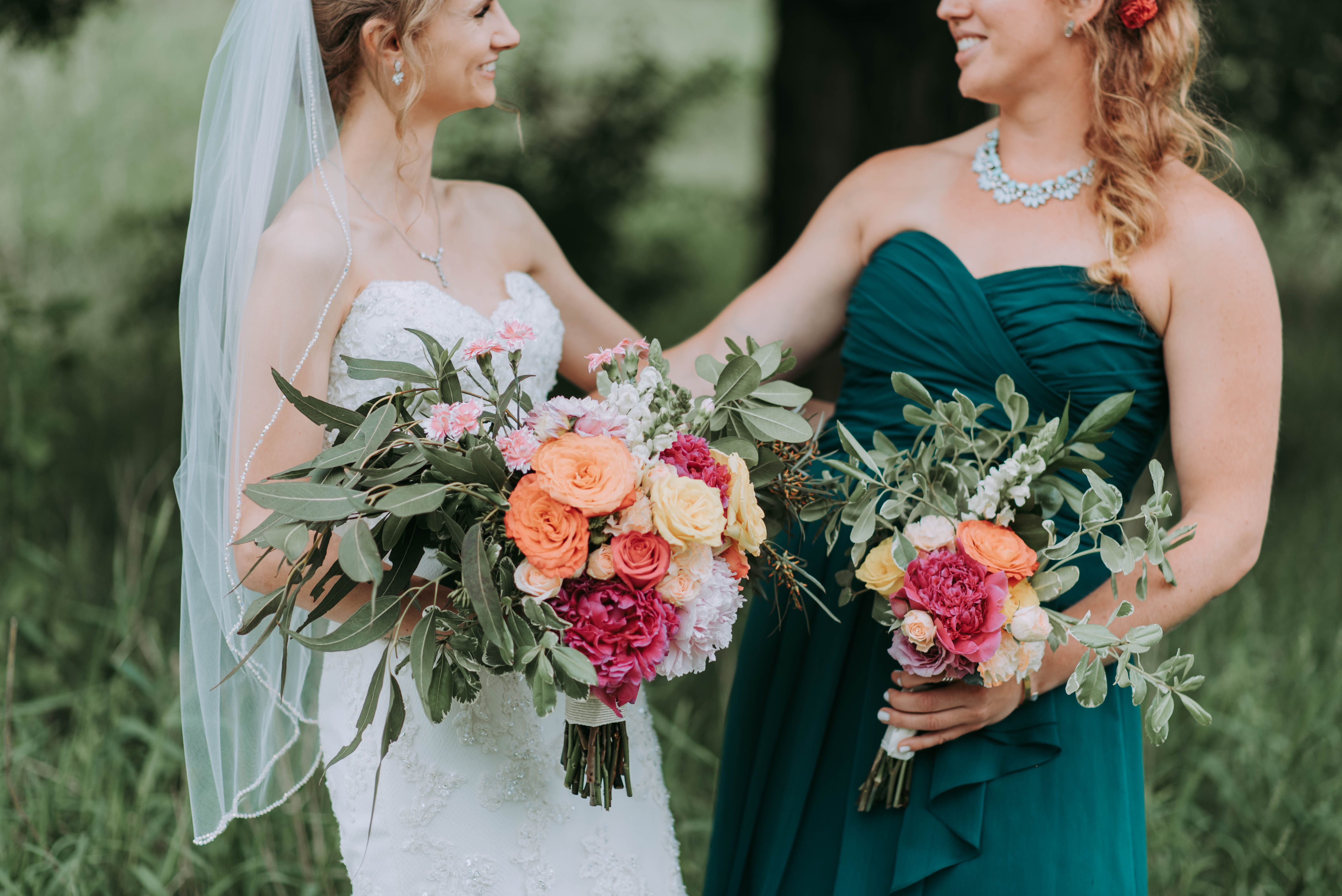 Maid of honor in green bridesmaid dress and bride in veil looking at each other smiling casually