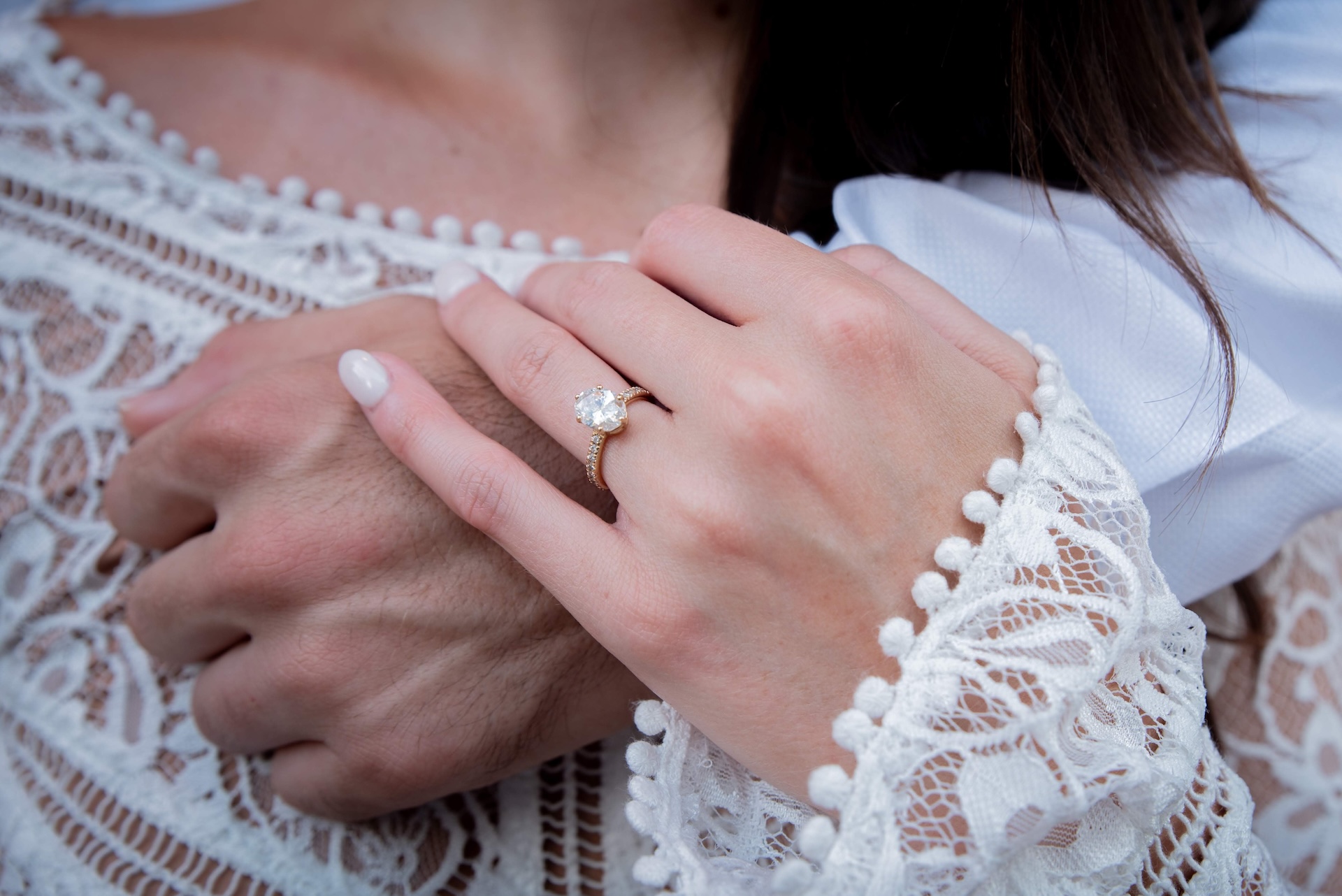 Close up of female hand with engagement ring holding male hand across her chest