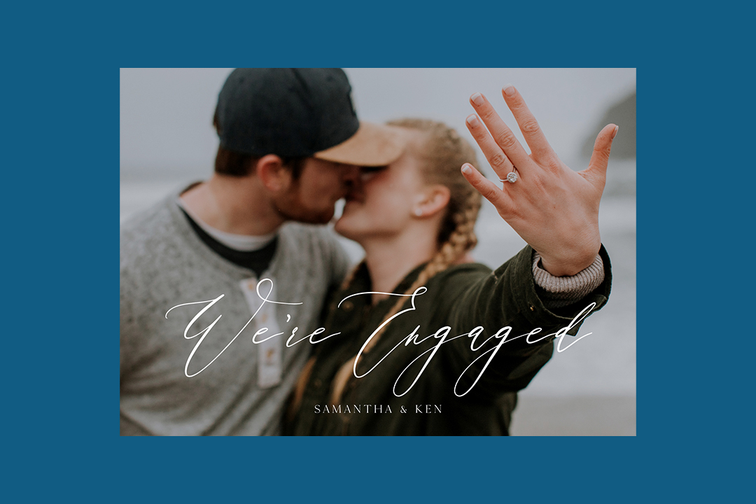 Couple kissing and showing engagement ring to camera in an engagement announcement photo card.