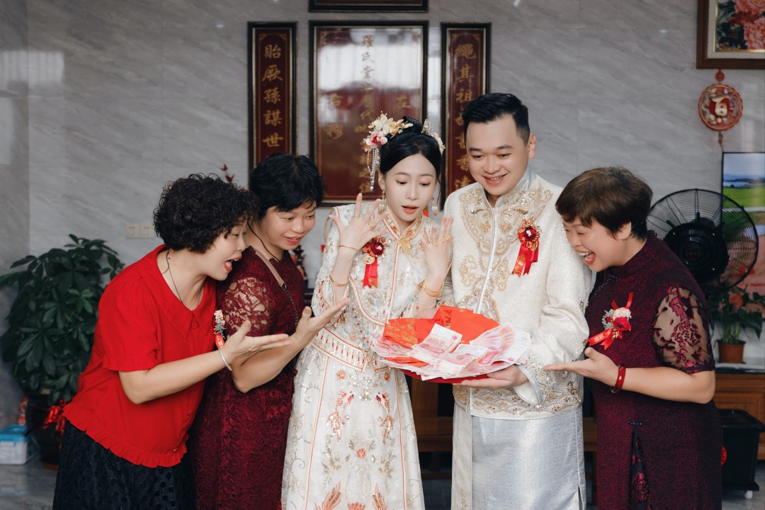 Asian family with bride and groom looking down at a paper and smiling
