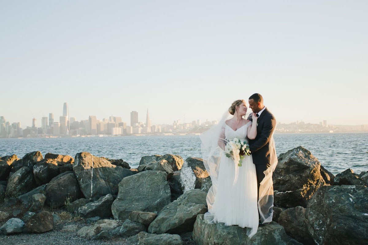 married couple taking wedding photo on San Francisco bay coast