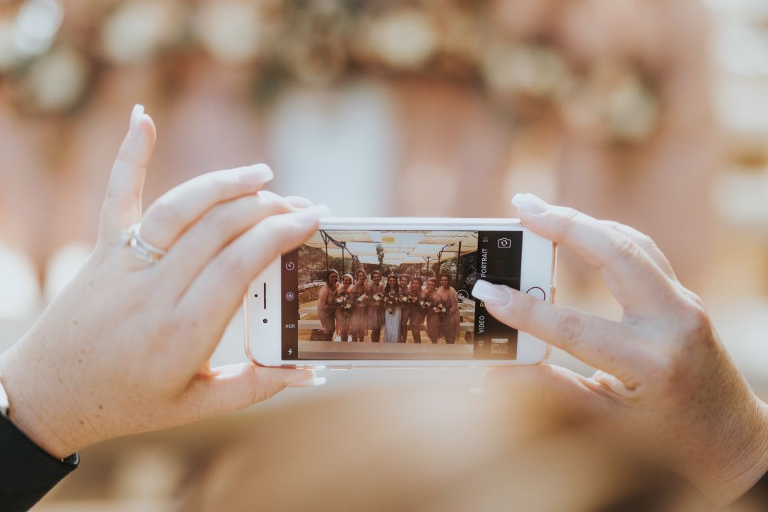 Woman holding iPhone taking picture of bride and her bridesmaids