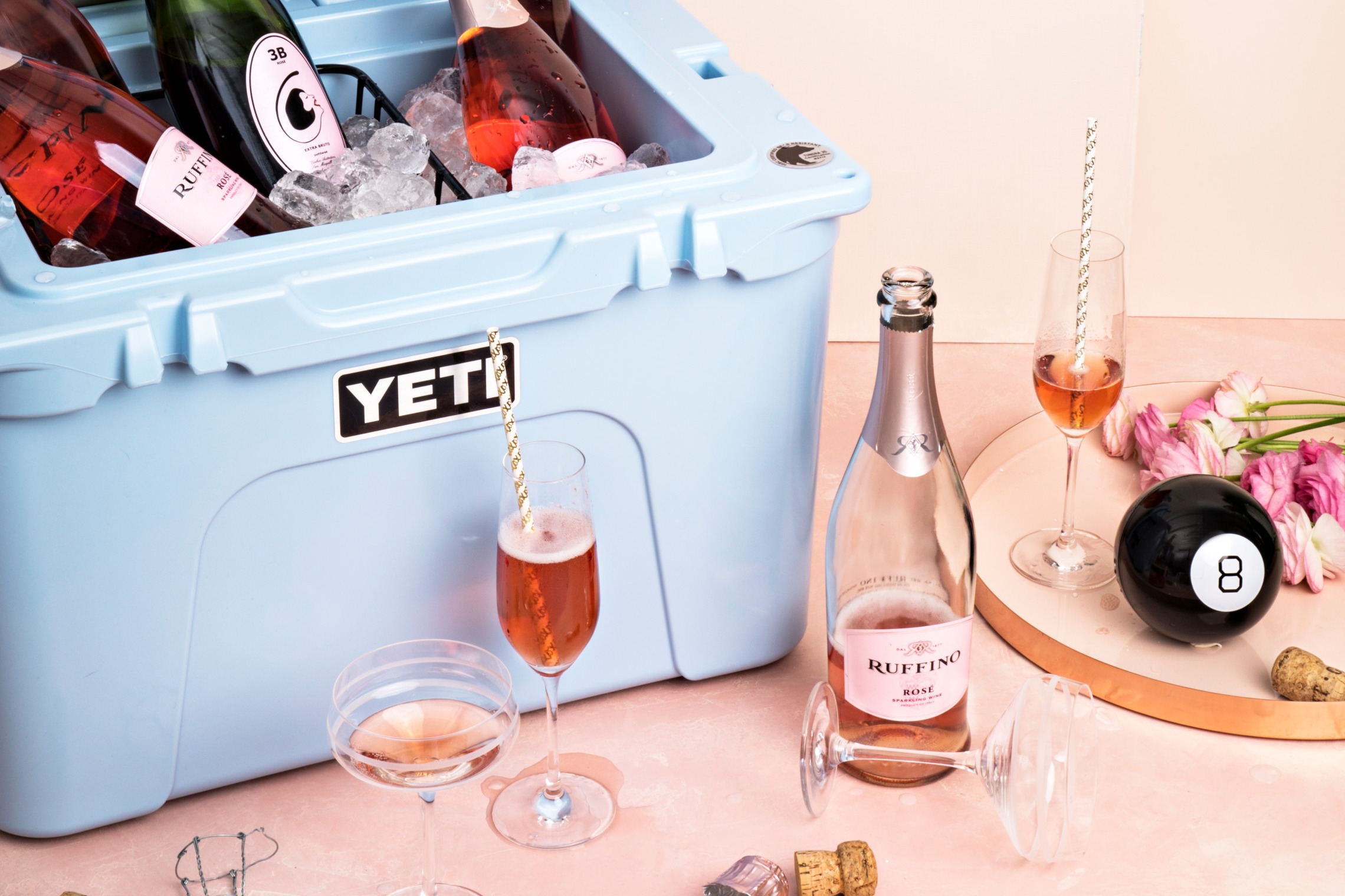Yeti cooler filled with bottles of sparkling rose wine and glasses filled with wine in the background
