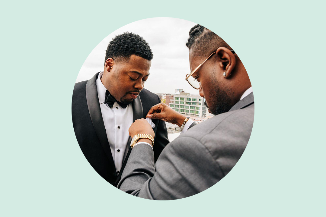 best man adjusts collar pin for groom in military attire