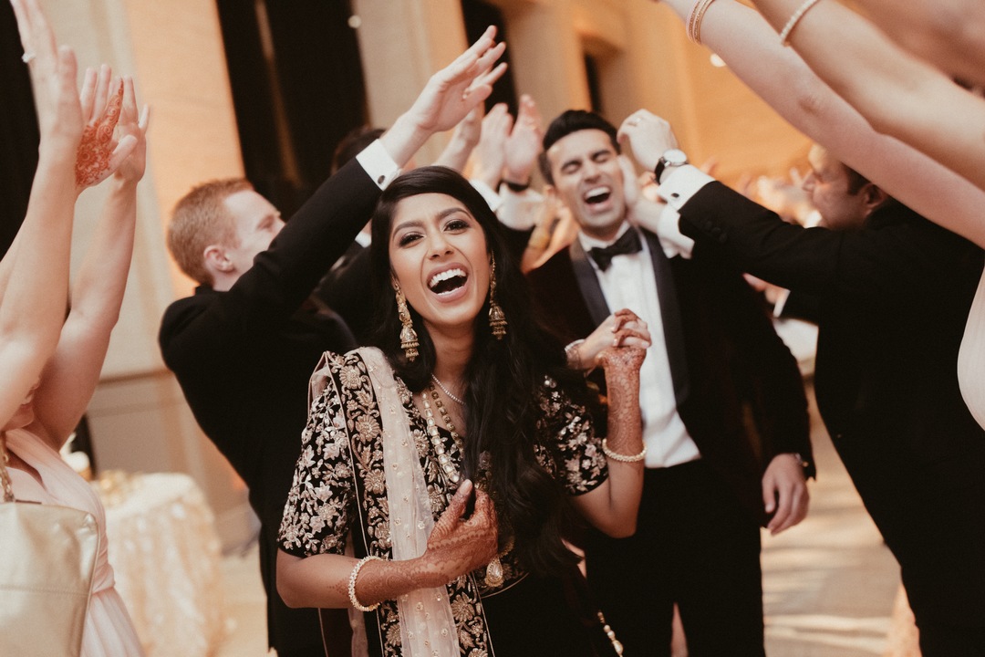 Couple smiling and laughing as they run through a line of guests with their arms up in the air celebrating