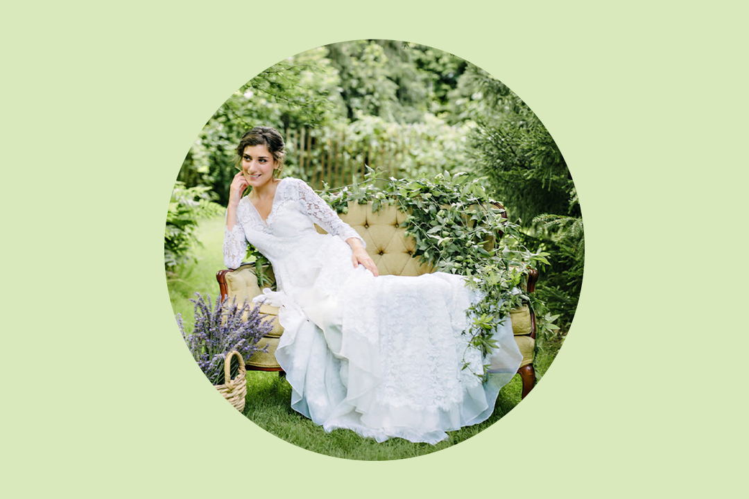 bride wearing long-sleeve lace dress sitting on a settee in the middle of a garden with a basket of cut purple lavender beside her