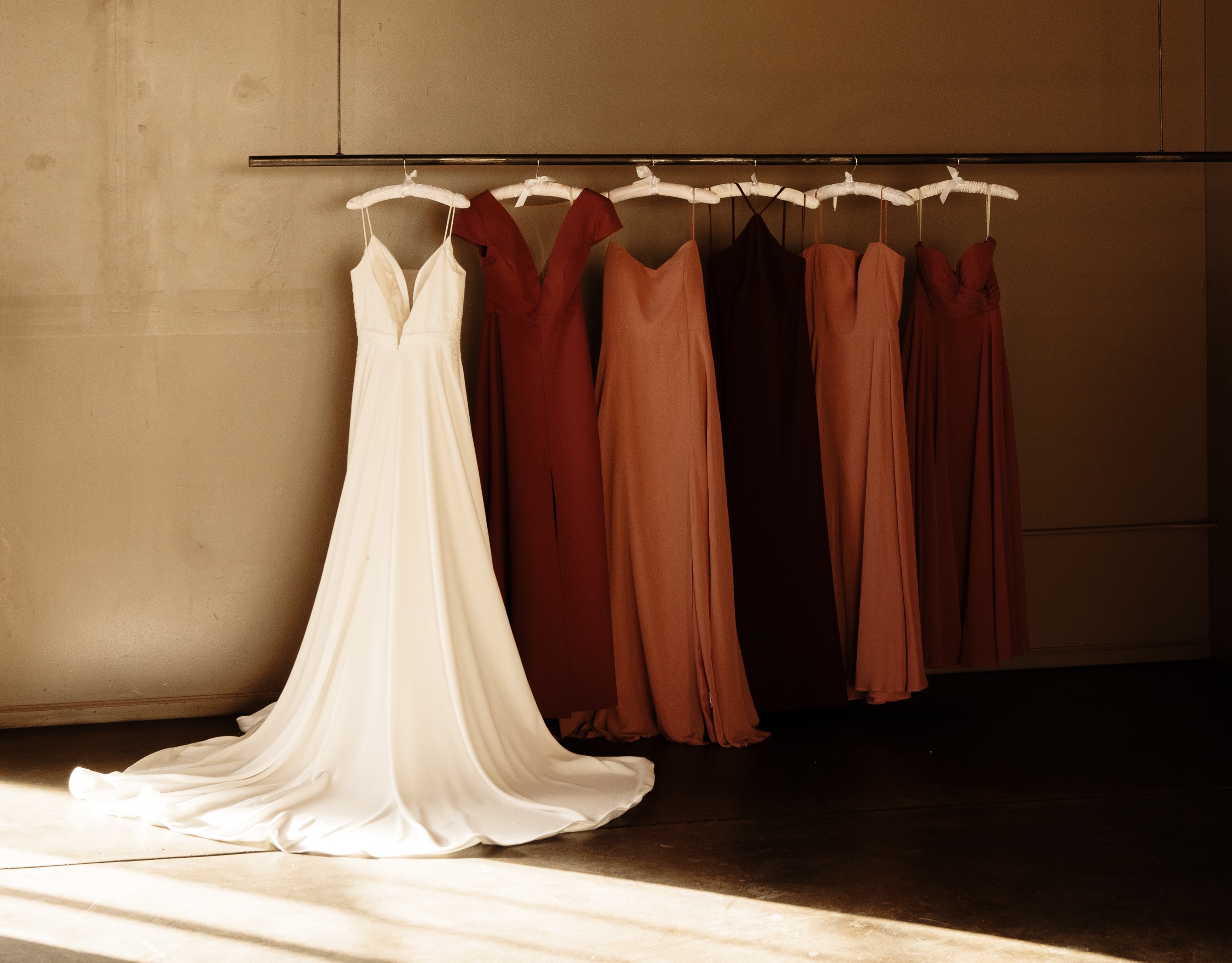 Wedding gown and four bridesmaids dresses in shades of red all hanging on a wall