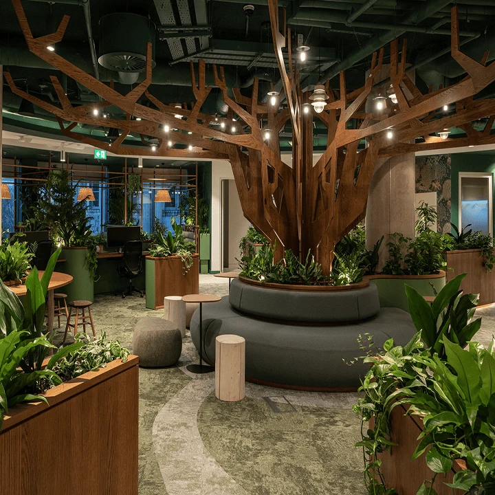 Ofisin iç mekanının fotoğrafı; odanın ortasında, oturma alanına bağlanan bir ağaç tasarımı bulunuyor.