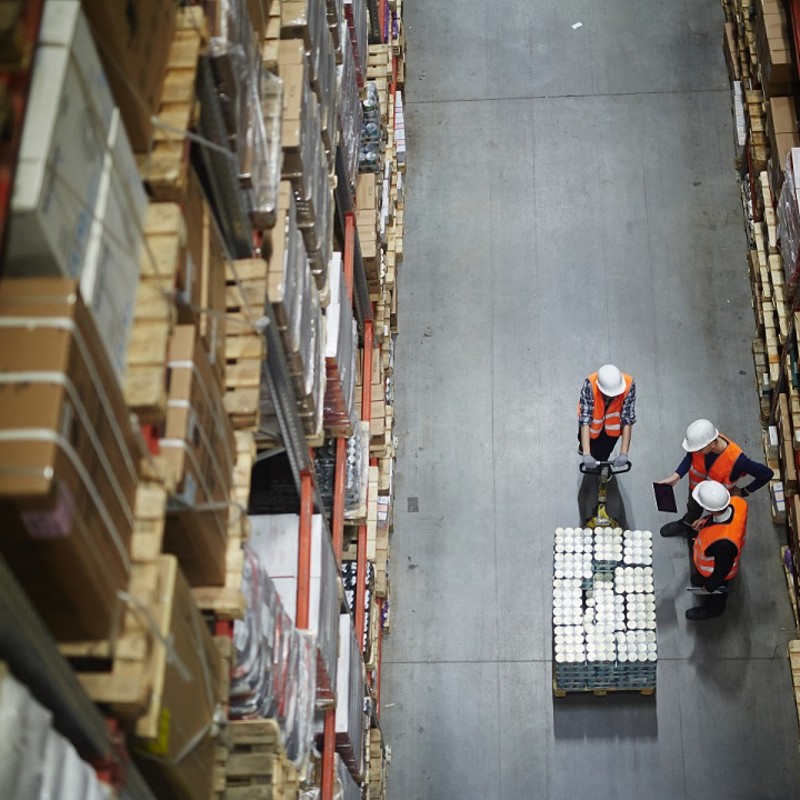 Warehouse workers looking at an iPad and talking in the aisle of the warehouse.