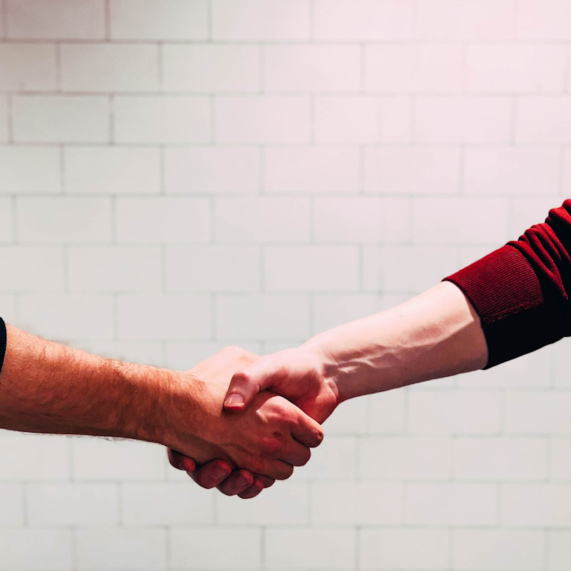 Two men shaking hands, with a white brick wall in the background.