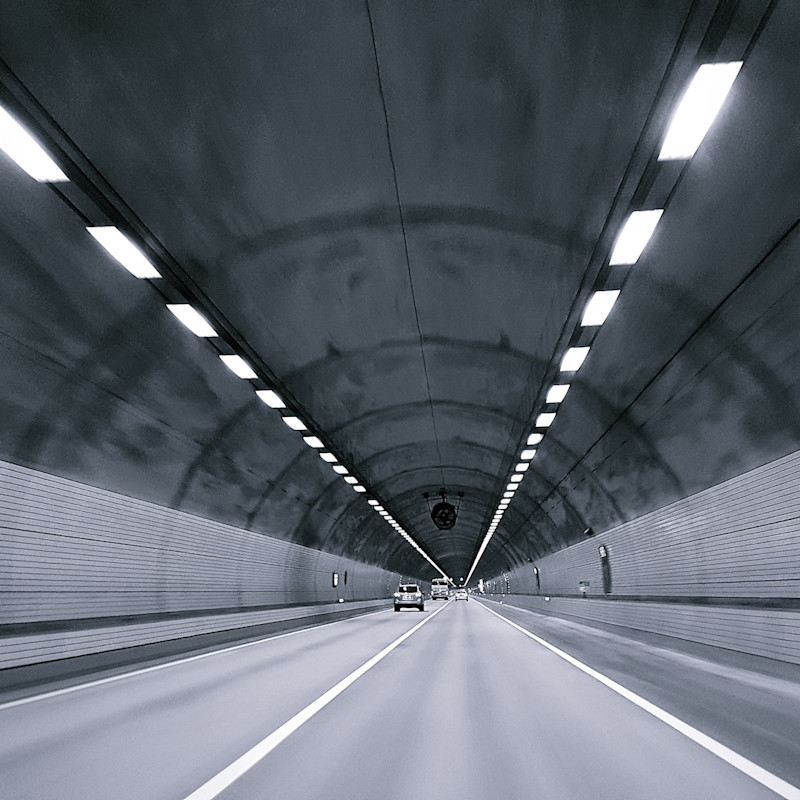 Grey and white photograph of a motor tunnel with cars driving down it.