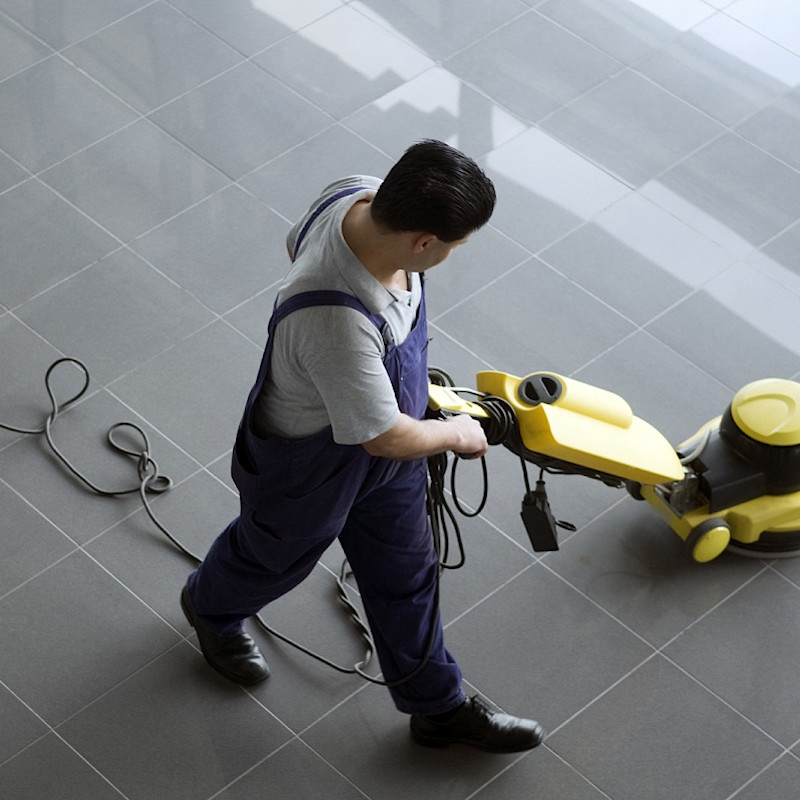 Cleaner cleaning a tiled floor in a building foyer.
