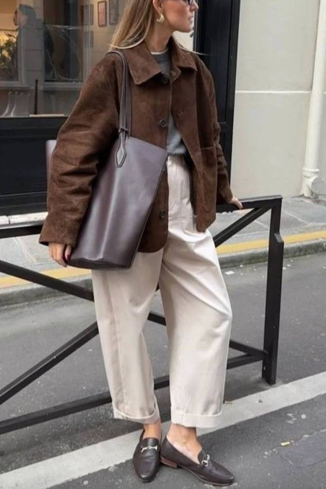 Street style image of women wearing brown outfit in september. Wearing a suede bomber jacket with a grey knit and barrel leg jeans with brown leather loafers