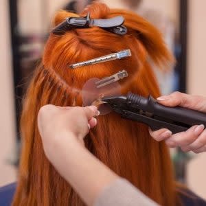 The hairdresser does hair extensions to a young, red-haired girl, in a beauty salon. Professional hair care. Bonding Extensions anbringen