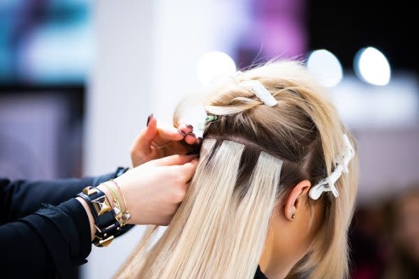 Professional hairdresser making hair extensions for blonde girl in a beauty salon Tape Extensions