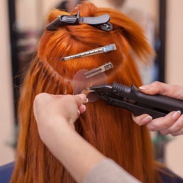 The hairdresser does hair extensions to a young, red-haired girl, in a beauty salon. Professional hair care. Bonding Extensions anbringen