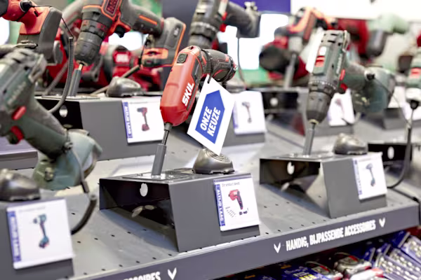 Diverse elektrische gereedschappen op display in de GAMMA bouwmarkt, waaronder een rode boor, gerangschikt op metalen standaards met productlabels.