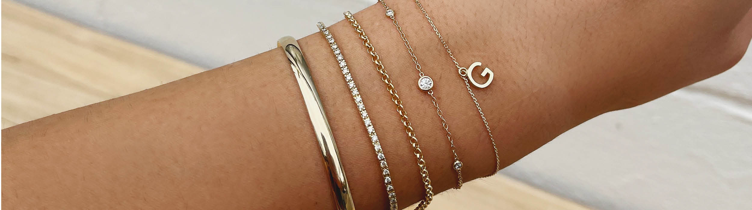 Five yellow gold bracelets stacked on a wrist