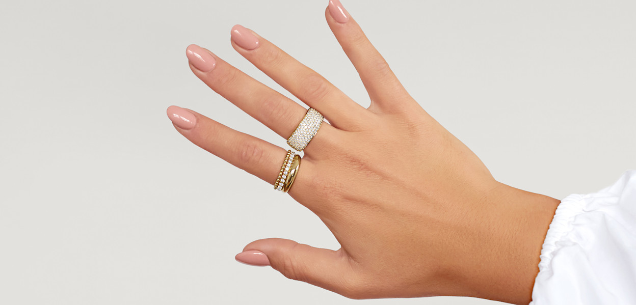 Female hand with statement diamond ring, a narrow diamond ring and more dainty diamond rings, all stacked together.