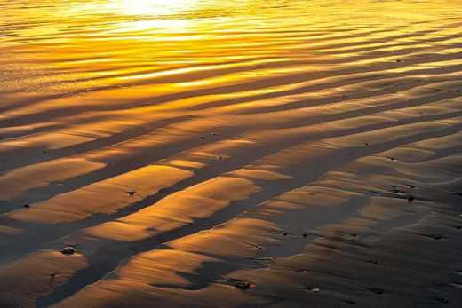 Photograph of wet sand reflecting sunset.