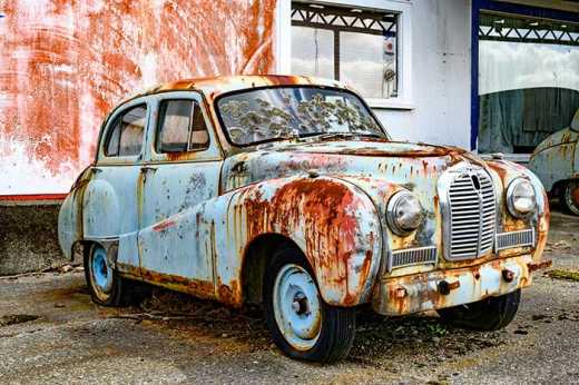Photograph of old rusting car with flat tires.