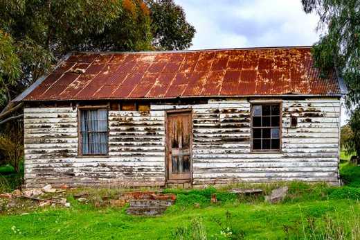 Photograph of severely weathered house with flaking paint and rusted roof.