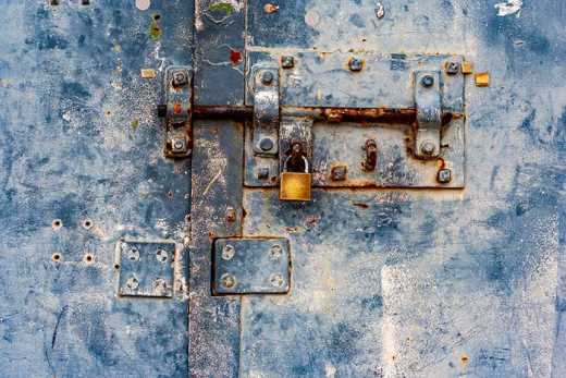 Photograph of rusted bolt and padlock on metal door.