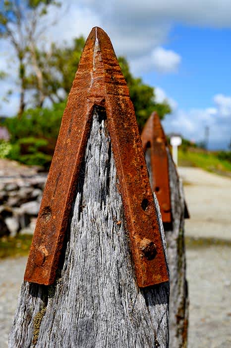 Photograph of crude rusty spear like caps on top of jetty posts.