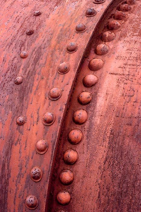 Photograph of part of old steam boiler (a curve of bolts).