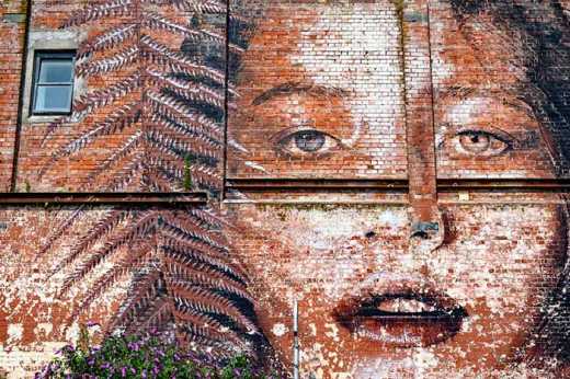 Photograph of large scale street art on brick wall of woman's face.
