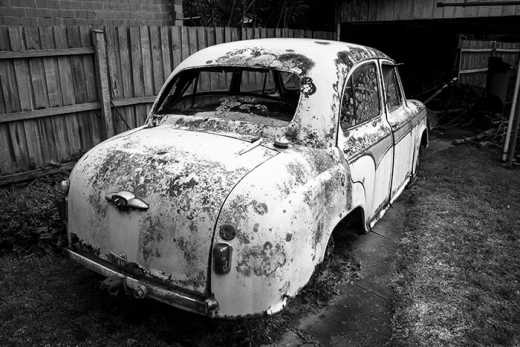 Photograph of old rusting car in suburban backyard.